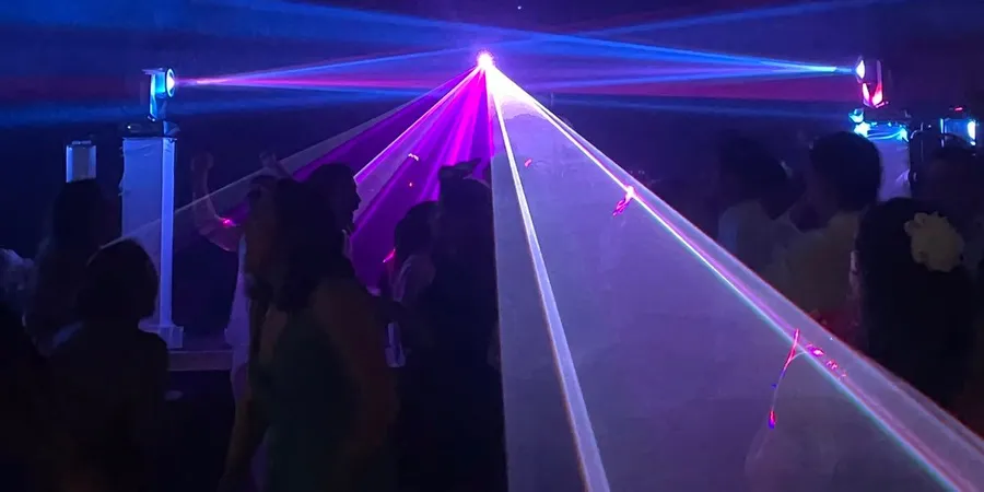 Piste de danse dans la nuit, invités sous les faisceaux laser violets et les lyres