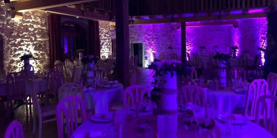Salle de dîner aux murs de pierre éclairés en violet, tables rondes nappées de blanc et centres de table fleuris